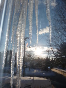 View from inside a Marlborough, MA home looking out a window at large icicles hanging from the roof eave, indicating a potential ice dam.